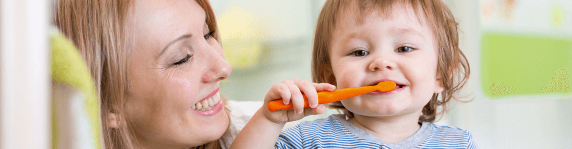 Mom holding toddler while he brushes his teeth 
